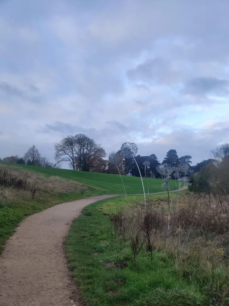 A curved pathway through the meadow, with wire dandelion sculptures running alongside.